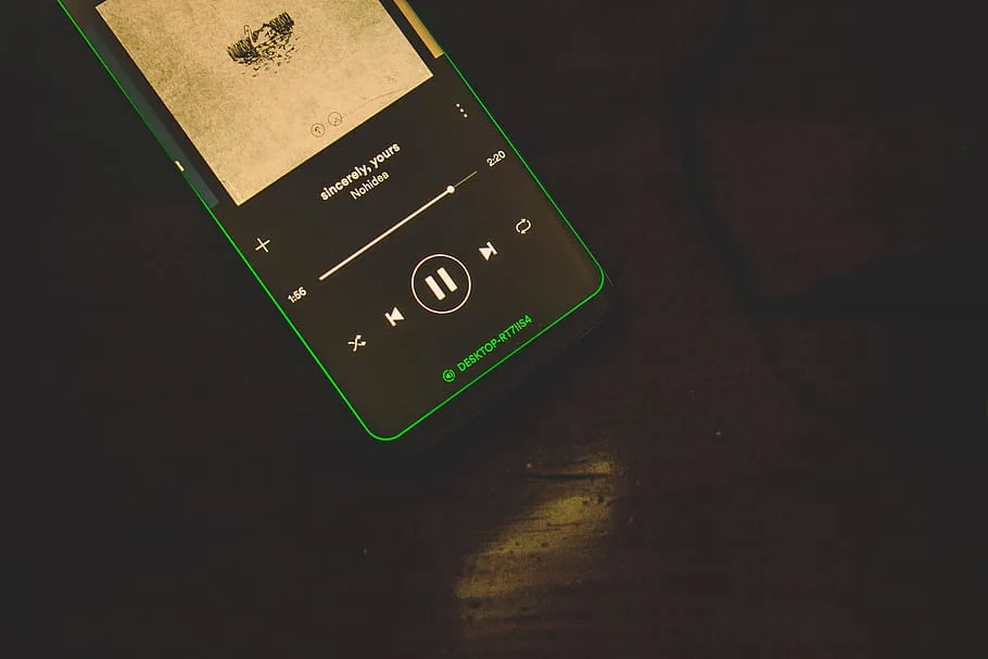 Mobil ležící na tmavém stole s přehrávanou skladbou ve Spotify